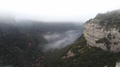 Misty-canyon-in-Osona,-Barcelona-with-fog-over-dense-forests-and-steep-cliffs,-wide-aerial-view