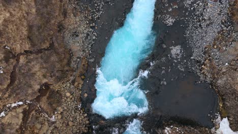 Turquoise-waters-flow-through-Bruarfoss,-the-blue-waterfall-in-Iceland,-aerial-view