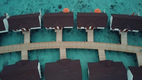Drone-top-down-video-of-a-tropical-resort-in-the-Maldives,-blue-lagoon,-sunny-weather,-turquoise-shallow-water,-water-villas,-island-wooden-road,-4K