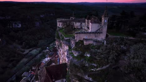 An-orbital-drone-shot-of-Rocamadour-santctuary,-starting-in-the-chateau-and-ending-down-the-cliff