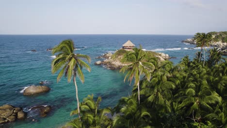 Aerial-orbiting-shot-of-Pristine-turquoise-water-from-Cabo-San-Juan,-beach-hut-through-lush-palm-trees,-Colombia