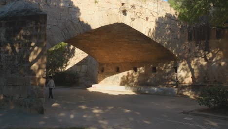 People-Walking-Under-The-Puente-del-Mar-Bridge-During-Sunny-Day-Over-The-Turia-River-Park-In-Valencia,-Spain