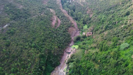 Sant-miquel-del-fai-with-lush-greenery-and-river-running-through-rocky-terrain,-barcelona,-aerial-view