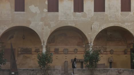 Una-Mujer-Camina-En-Una-Arquitectura-Histórica-Con-Un-Pasaje-Cubierto-De-Arcos-En-Venecia,-Italia