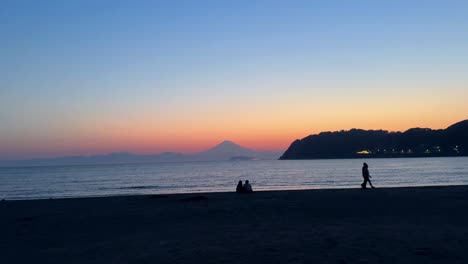 Silhouette-of-people-on-a-beach-at-sunset-with-distant-mountain,-tranquil-and-serene