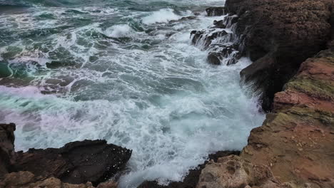 Waves-crash-with-force-against-a-cliffside,-splashing-white-foam-over-the-rocky-edge,-captured-in-dramatic-slow-motion