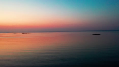 Drohne-Senkt-Sich-über-Ruhigem,-Wunderschönem-Meeressonnenaufgang-Mit-Kleinen-Inseln-Am-Horizont