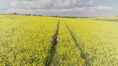 Young-woman-running-through-field-of-yellow-and-green-foliage,-aerial