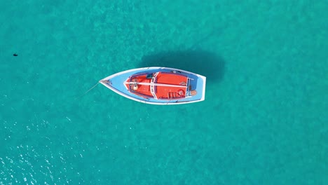 Orange-sailboat-with-blue-deck-anchored-in-turquoise-Caribbean-ocean-water,-drone-descend