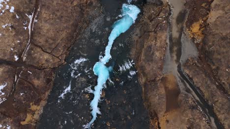 Luftaufnahme-Des-Atemberaubenden-Bruarfoss-Wasserfalls-In-Island,-Der-Leuchtend-Blaues-Wasser-Zeigt,-Das-Sich-Durch-Dunkle-Felsen-Schlängelt