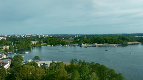 A-panoramic-view-of-Ukiel-Lake,-bordered-by-dense-greenery-and-a-developed-urban-area,-under-a-clear-sky