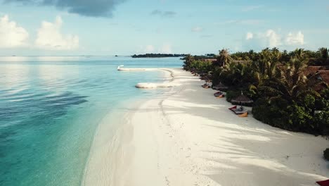 Drohnenvideo-Eines-Tropischen-Resorts-Auf-Den-Malediven,-Niedriger-Flug,-Blaue-Lagune,-Grüne-Palmen,-Sonniges-Wetter,-Türkisfarbenes-Flaches-Wasser,-Bunte-Sonnenliegen,-4k