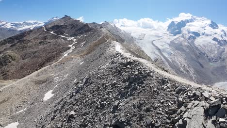 Flight-over-a-hiking-trail-at-Alps-mountains-in-Gornergrat,-Zermatt,-in-Switzerland-with-the-reveal-view-of-a-beautiful-glacier