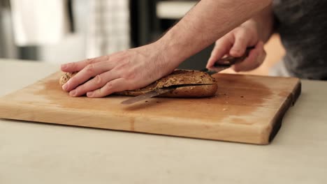 White-man-slicing-through-brown-baguette-with-serrated-knife-on-kitchen-countertop