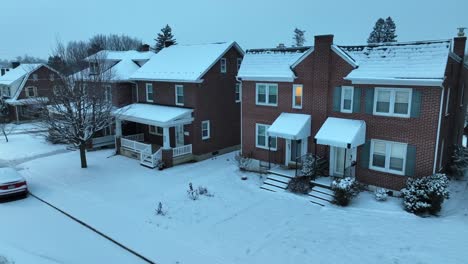 Twilight-scene-of-a-snowy-suburban-street-with-red-brick-houses,-snow-covered-roofs,-and-cars-parked-alongside