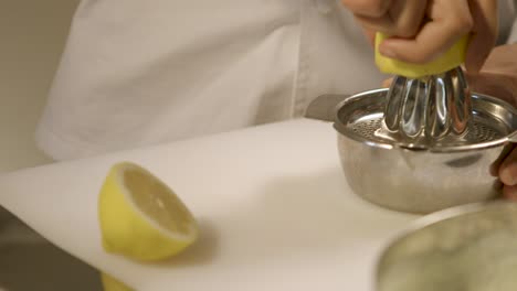 Chef-squeezing-lemon-juice-into-a-stainless-steel-bowl,-focused-on-hands-and-fruit,-kitchen-setting,-panning-shot