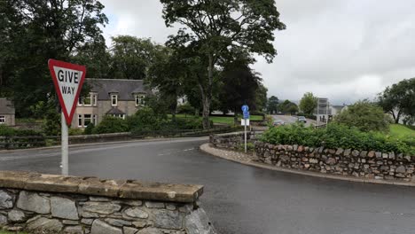 Give-way-traffic-sign-at-T-junction-in-Dufftown,-Scotland-with-cars-driving-by-after-rain