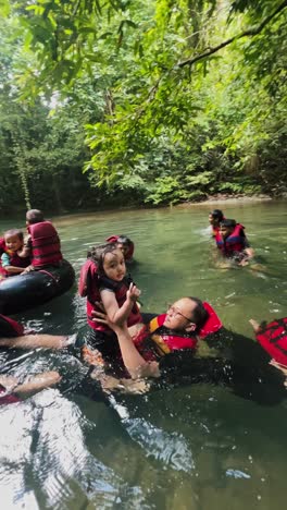 Row-of-floating-people-in-the-mountain-river-when-on-vacation-with-little-girl-waving-hand-to-a-camera