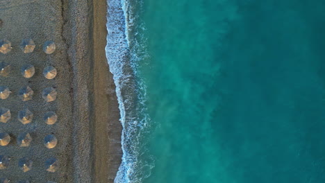 Drone-Aéreo-De-Arriba-Hacia-Abajo-Disparado-Sobre-Las-Sombrillas-De-Playa-A-Lo-Largo-De-La-Costa-De-Corinto,-Kiato,-Grecia-Durante-El-Día