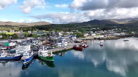 Drone-small-fishing-boat-leaving-Castletownbere-harbour-Ireland-with-large-boats-preparing-to-go-to-sea-on-a-bright-summer-morning