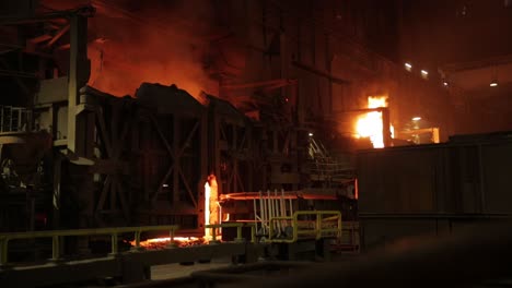 Intense-industrial-scene-with-molten-metal-and-fiery-furnaces-at-a-steel-mill-at-night,-showcasing-a-glowing,-ominous-atmosphere