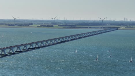 Drohnenaufnahme-Der-Zeelandbrücke-Mit-Langem-Objektiv,-Im-Hintergrund-Sind-Segelboote-Und-Ein-Großer-Hafen-Zu-Sehen