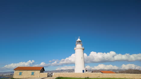 old-lighthouse-in-Pafos,-Cyprus,-standing-tall-against-a-striking-blue-sky-dotted-with-fluffy-clouds