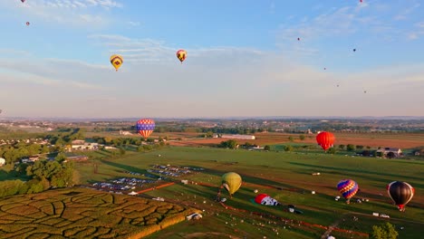 Luftaufnahme-Von-Bunten-Heißluftballons,-Die-In-Den-Frühen-Morgenhimmel-über-Einer-Ruhigen-Ländlichen-Landschaft-Aufsteigen