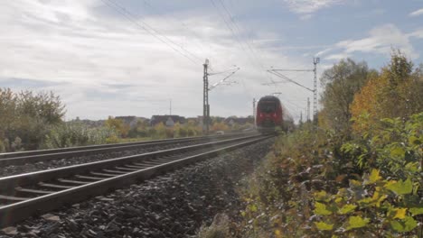 Red-Deutsche-Bahn-train-speeding-through-a-rural-track-on-a-sunny-autumn-day,-with-bright-foliage