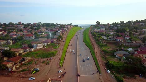 Kampala-Entebbe-Expressway,-Uganda,-East-Africa---Vehicles-Traveling-on-the-Road-Bordering-a-Residential-Area---Drone-Flying-Forward