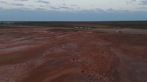 Drone-clip-showing-truck-with-multiple-carriages-driving-along-straight-road-through-Australian-outback