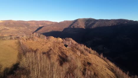 Aerial-drone-shot-of-a-wooden-cabin-in-the-wild-forrest-of-Transilvania,-Romania-on-a-sunny-day-with-clear-sky-golden-hour