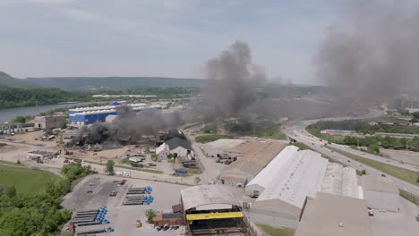 Amplia-Panorámica-Aérea-A-Través-De-Una-Carretera-Muy-Transitada-Con-Un-Gran-Incendio-Industrial-En-El-Que-Los-Servicios-De-Emergencia-Están-Trabajando