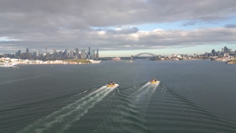 Dos-Taxis-Acuáticos-Que-Cruzan-El-Puerto-De-Sydney-Con-El-Puente-Del-Puerto-Y-La-ópera-Al-Fondo.