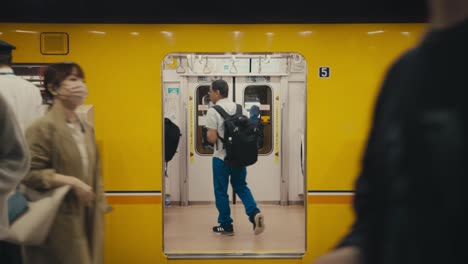 Viajeros-Caminando-En-La-Estación-De-Metro-De-Tokio,-Japón,-Con-Un-Tren-De-Pasajeros-Al-Fondo.