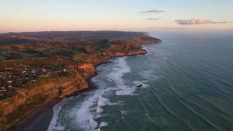 Aerial-View-of-the-Coastline-Of-Muriwai-Coastal-Community-In-Sunset-In-Auckland,-New-Zealand