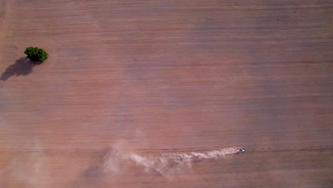 Aerial-top-down-tracking-follows-tiny-tractor-ploughing-with-dust-cloud-trailing-behind