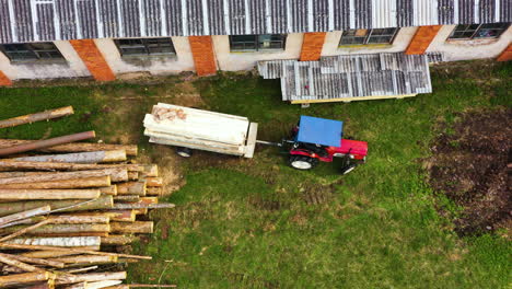 Tractor-backs-up-trailer-of-milled-plank-logs-on-side-of-sawmill,-aerial-top-down-static