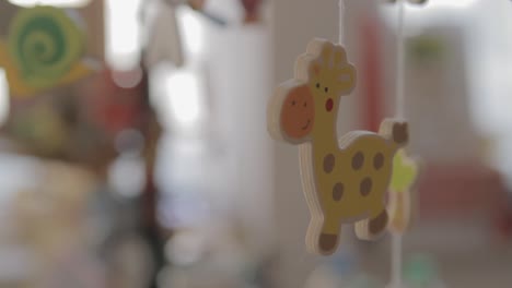 Blurry-close-up-of-a-colorful-giraffe-wooden-mobile-in-a-softly-lit-child's-room