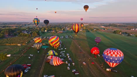 Eine-Flotte-Lebhafter-Heißluftballons-Erhebt-Sich-Sanft-In-Einen-Warmen-Sonnenuntergangshimmel-über-Einer-Ruhigen-Ländlichen-Landschaft