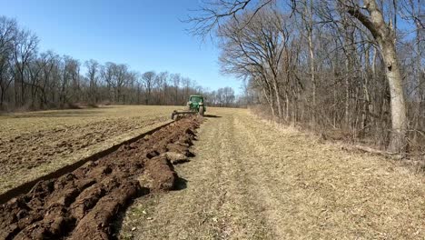 Following-an-agricultural-tractor-towing-a-plow-through-a-empty-field-in-early-spring-in-Midwest