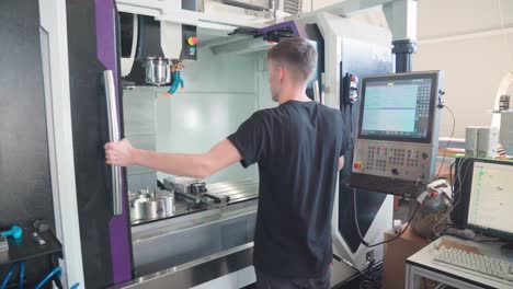 Operator-closing-the-door-of-vertical-CNC-machining-center-and-preparing-computer,-estbalisher