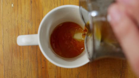 Pouring-Fresh-Black-Coffee-From-Glass-Jug-Into-White-Cup,-Top-Down-View