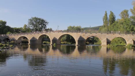 Tranquil-scene-of-an-ancient-stone-bridge-reflecting-in-calm-water-on-a-sunny-day