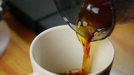 Pouring-Fresh-Black-Coffee-From-Glass-Pot-Into-White-Cup-In-Kitchen,-Close-Up