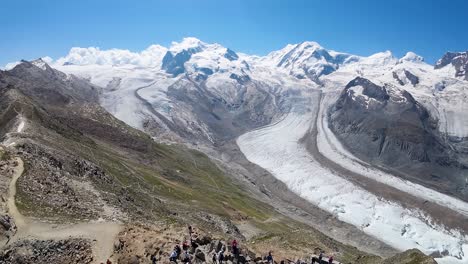 Flight-over-the-observatory-at-Gornergrat,-Swiss-Alps-mountains-in,-Zermatt,-Switzerland-with-the-reveal-view-of-a-beautiful-glacier-getting-shorter-due-to-climate-change-or-global-warming