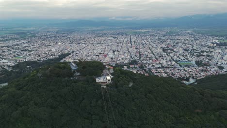 Luftbild-Mit-Haus-Auf-Dem-Berggipfel-Im-Vordergrund,-Hauptstadt-Von-Salta-Im-Hintergrund