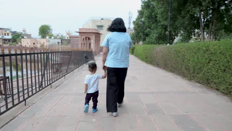 young-mother-holding-toddler-son-finger-and-walking-at-outdoor-at-evening