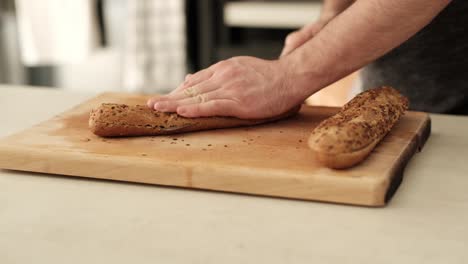 Man-slicing-healthy-baguette-on-wooden-chopping-block-on-the-kitchen-countertop