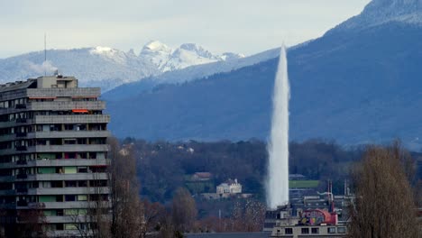 A-shot-of-the-Jet-d´Eau-in-Geneva,-with-a-building-at-the-left-of-the-shot-and-the-alps-in-the-background